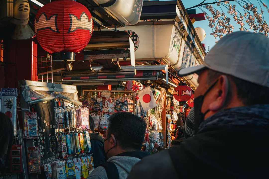 Warm side light on red chochin lanterns, folk-craft stalls and early cherry blossom.