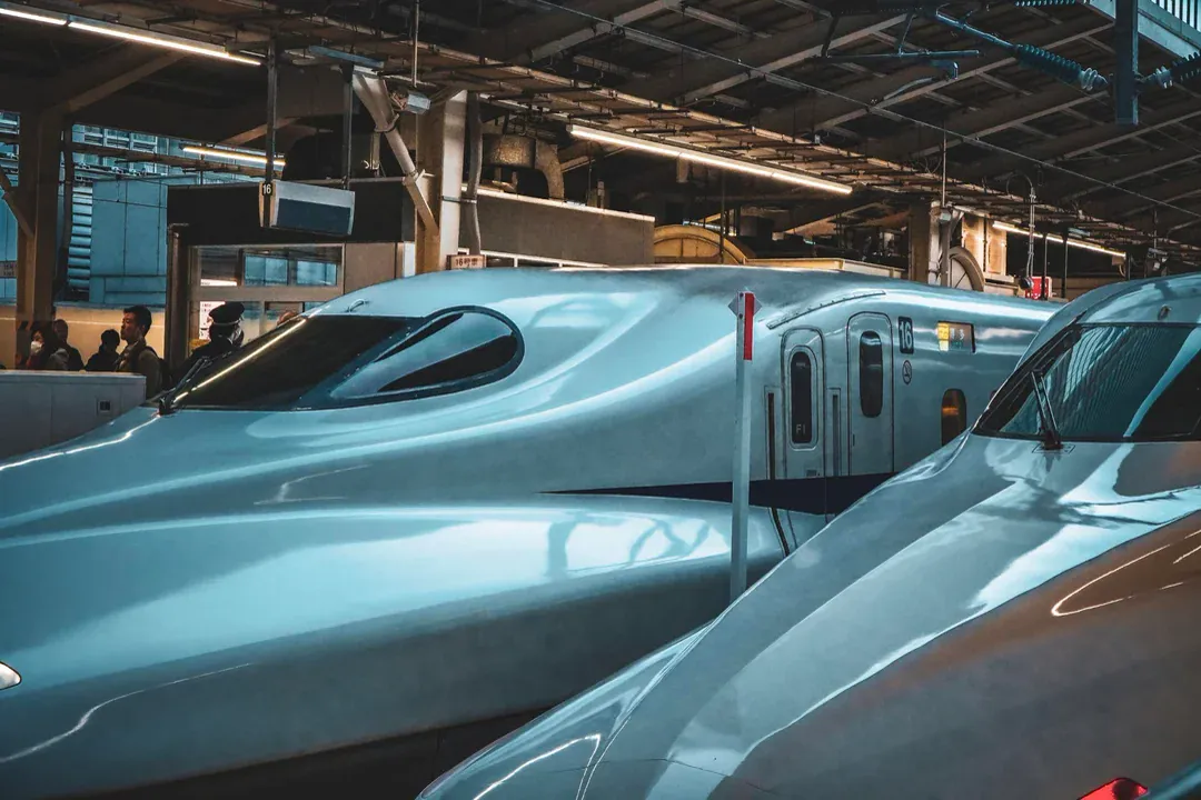 The sculpted nose cones of N700S bullet trains resting beneath steel station trusses.
